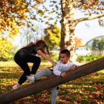 Two kids enjoying playtime on a seesaw in an autumn park with colorful leaves.